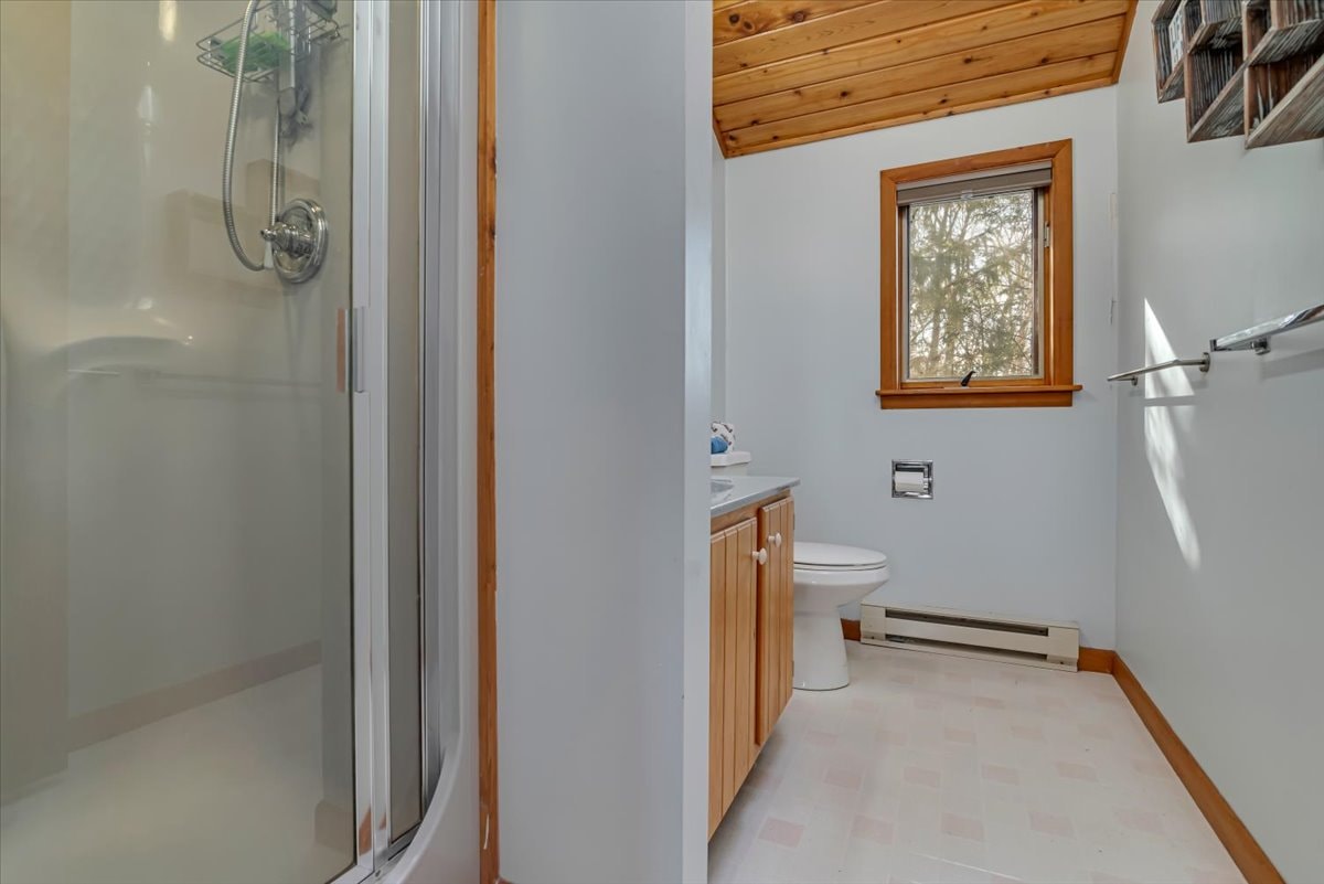 Bathroom with glass shower, pine wood ceiling and forest window view